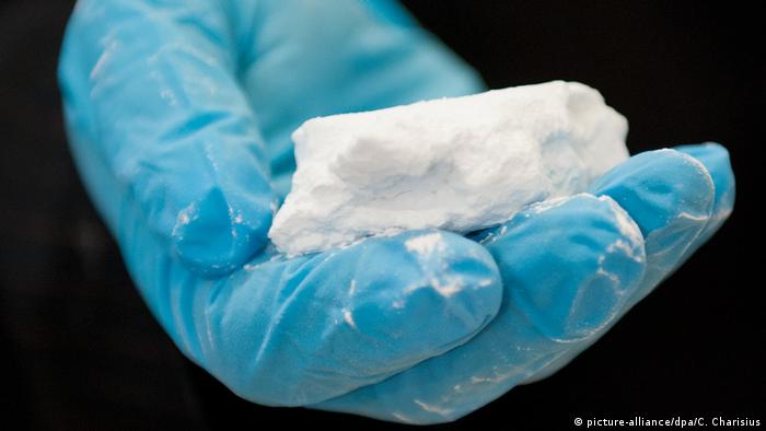 Foto de mano con guante azul sosteniendo polvo blanco que simboliza cocaína