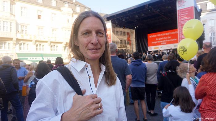 Beethoven-Fest Bonn 2018 (DW/M. Webber) Woman wearing a white button-up shirt smiles at the camera with the stage behind her in Bonn main square. 