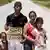 Família de refugiados venezuelanos em Roraima posa para foto na estrada, com pai segurando papelão com as palavras "SOS Venezuela"