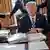 Дональд Трамп за столом в Овальном кабинете, сзади его сотрудники