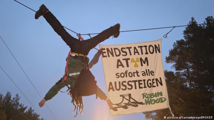 Ein Mensch hängt über einer Bahnline, neben ihm ein Protestplakat gegen die Atom-Transporte nach Gorleben