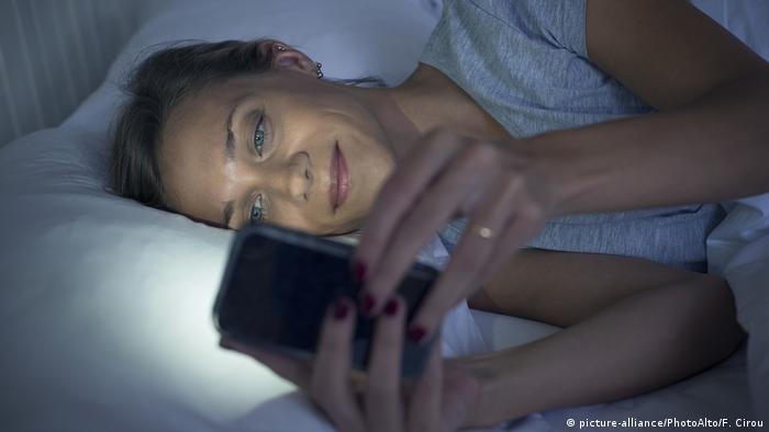 Frau benutzt Smartphone im Bett (picture-alliance/PhotoAlto/F. Cirou)