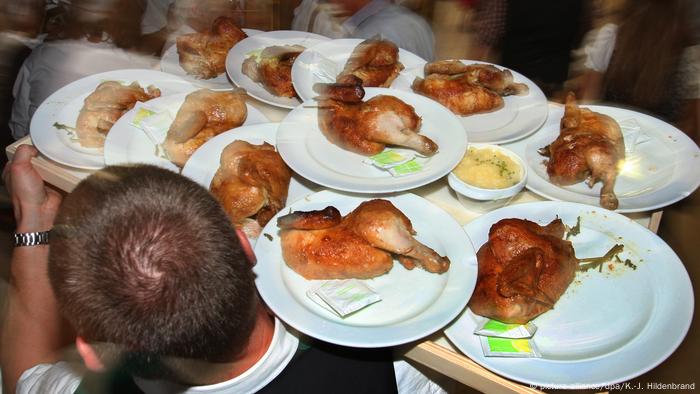 Un hombre lleva una bandeja llena de platos repletos de trozos de pollo asado y toallitas húmedas