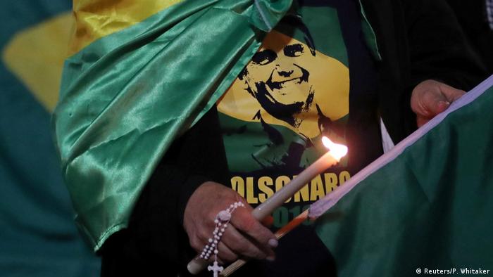 Apoiadora de Jair Bolsonaro veste camiseta de candidato e carrega vela acesa e terço