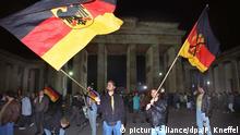 ARCHIV - Jugendliche schwenken in der Nacht zum 3. Oktober 1990 vor dem Brandenburger Tor in Berlin die Deutsche Fahne (l) und die Fahne der DDR, auf der das DDR-Emblem (Hammer und Zirkel) durchgestrichen ist. Mit dem Beitritt der DDR zur Bundesrepublik am 3. Oktober 1990 sind die Deutschen 45 Jahre nach dem Ende des 2. Weltkrieges wieder in einem souveränen Staat vereint. Am 03.10.2015 jährt sich die Deutsche Wiedervereinigung zum 25sten Mal. Foto: Peter Kneffel/dpa +++(c) dpa - Bildfunk+++ | Verwendung weltweit