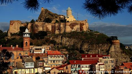 Historic buildings in the city of Tbilisi with a large temple on top of a rock.