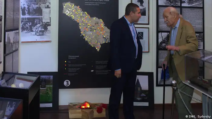 Kozlenko (left) speaks with Holocaust survivor Mihail Zaslavsky in front of a map showing the sites were Jews were executed