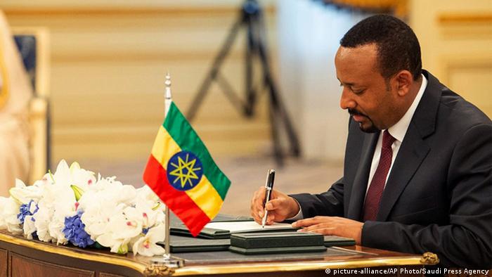 Ethiopian Prime Minister Abiy Ahmed looks down as he signs a peace deal with Eritrea. There are white flowers and the Ethiopian flag on top of the desk