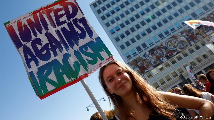 A woman holds a sign that reads: United against racism