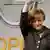 Angela Merkel waving in front of an Opel logo.