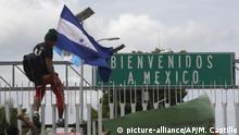 A Honduran migrant hold his national flag, climbs the border fence in Ciudad Hidalgo, Mexico, Thursday, Oct. 18, 2018. Migrants broke down the gates at the border crossing between Guatemala and Mexico and began streaming toward a bridge into Mexico. The road sign reads in Spanish Welcome to Mexico. (AP Photo/Moises Castillo) |