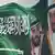 علم السعودية على حائط رسم عليه صورة الملك سلمان وولي عهده الأمير محمد