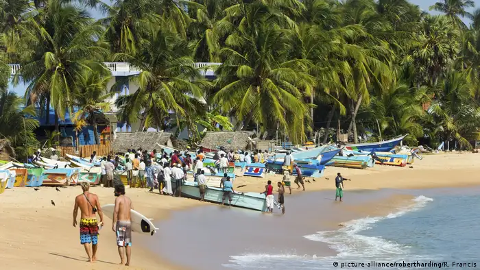 Tourists stroll as local fishermen work on a popular surf beach in Sri Lanka.