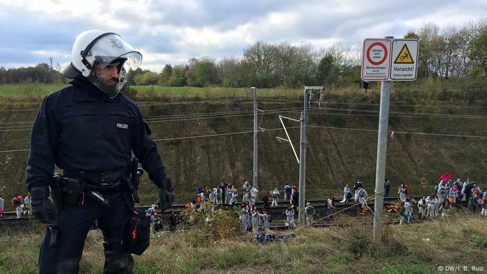 Un oficial de policía se para al borde de una colina.  Detrás de él, los manifestantes han llegado a la línea férrea del tren del carbón.