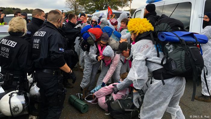 Un manifestante yace en el suelo después de caer.  Otros manifestantes la ayudan a ponerse de pie mientras los policías observan.