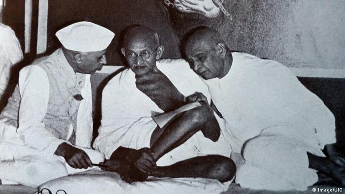 Mahatma Gandhi sitzend mit zwei Männern
