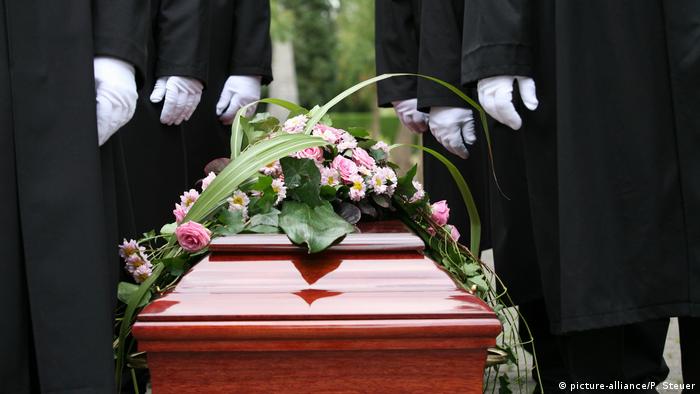Mrtvački sanduk s cvijećem i pogrebnici koji ga nose
