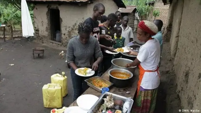 A woman dishes out food from metal pots for a group of people queing at an outdoor counter