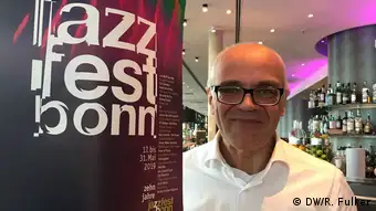 Peter Materna leans against a post in a hotel that has the jazzfest poster on it