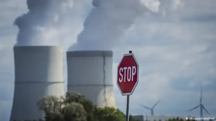 A stop sign in the foreground, while a coal power plant in the background spews out smoke