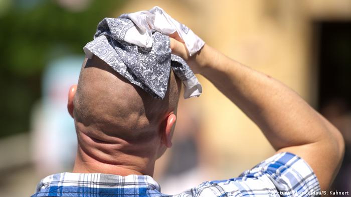 Man holding a rag to his head, sweating in a heatwave