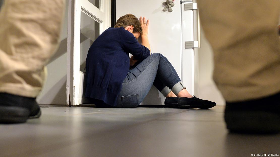 Žena sklupčana u uglu sobe i muškarac iznad nje