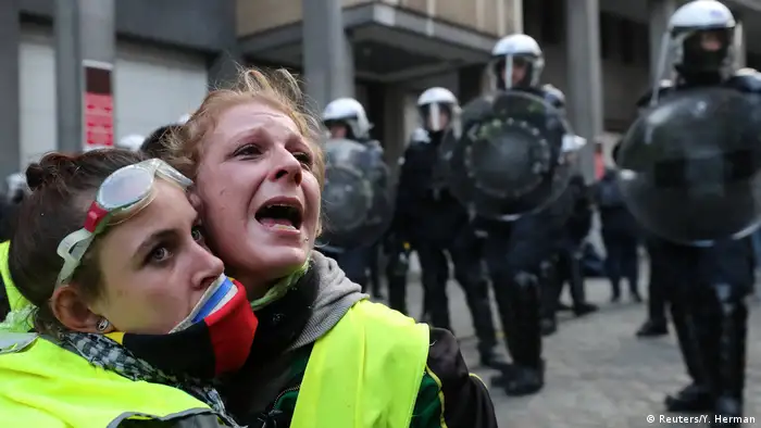 Two protesters in yellow vests cling to one another and cry out as police stand in the background (Reuters/Y. Herman)