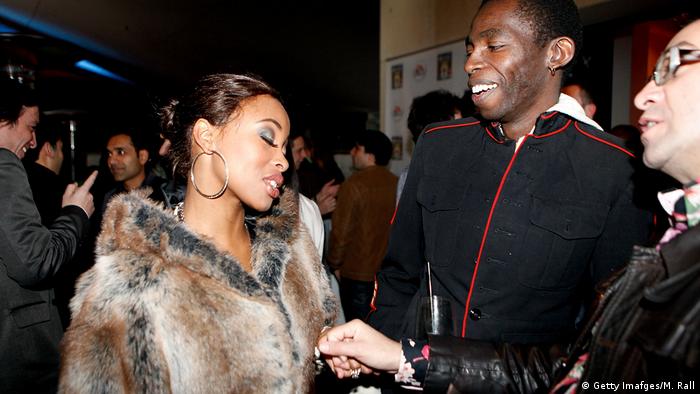 Khanyi Mbau in a fur coat and hooped earrings talks to two men (Getty Imafges/M. Rall)