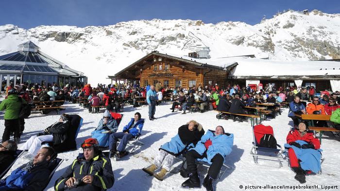 Skiers sit in the sun at the top of a mountain.