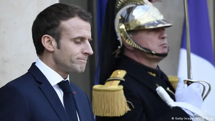 Macron presses his lips together and looks down as he stands next to a guard (Getty Images/AFP/B. Guay)