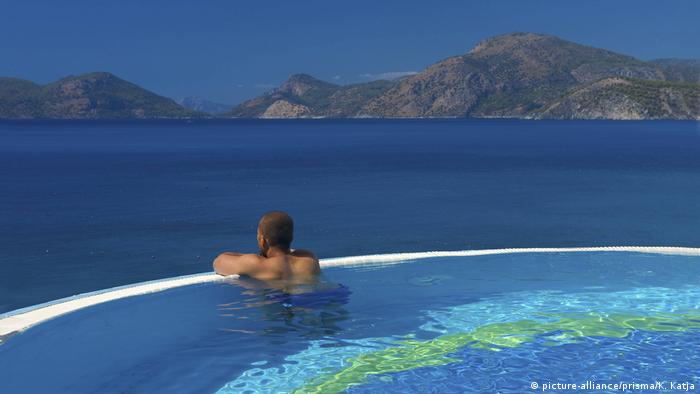 A man sits in a swimming pool overlooking the ocean.