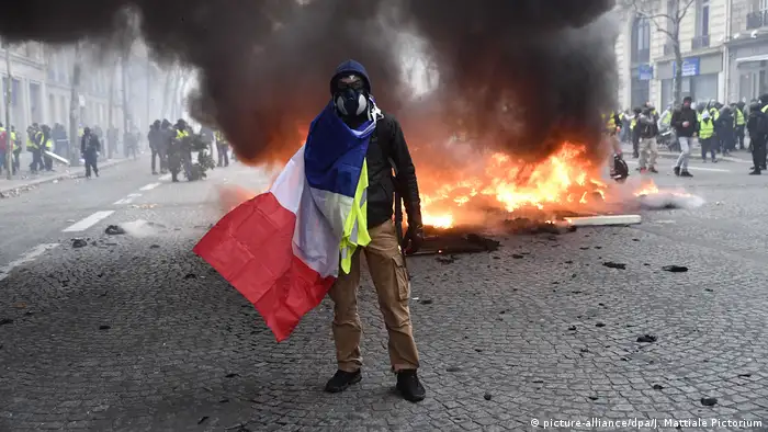 A man in a gas mask with a french flag stands in front of burning debris in Paris (picture-alliance/dpa/J. Mattiale Pictorium)