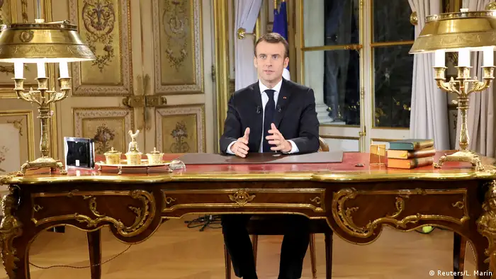 Macron sits at an elaborate desk and holds out his hands as he gives a televised address (Reuters/L. Marin)