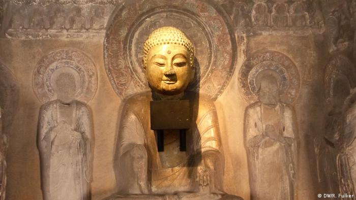 Golden Buddha head mounted on a wall and surrounded by sketched figures (DW/R. Fulker)