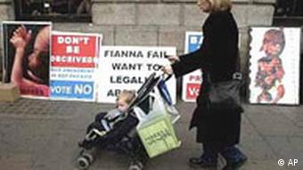 A woman with baby pram walks past pro and anti abortion posters