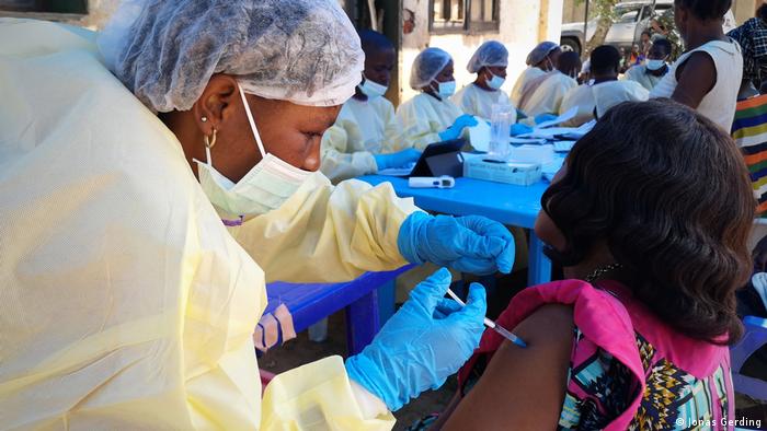 A health worker administers a vaccine to a woman. The health worker is wearing protective gear