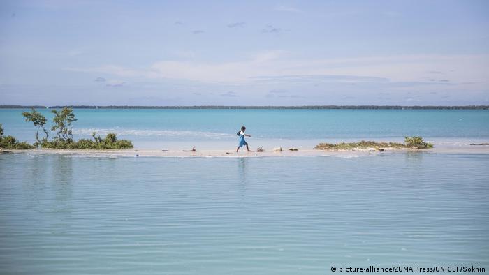 A boy walking to school during high tide in Kiribati