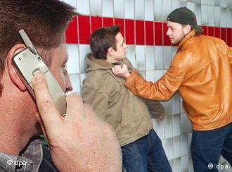A man makes a call on a cellphone while another man is pushed against a wall by an assailant