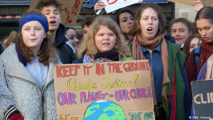 Teenagers shout as they take part in a climate protest in Cologne. The girl in the middle is wearing a cardboard sign around her neck which reads 'Keep it in the ground. Climate justice! Our planet - our choice'