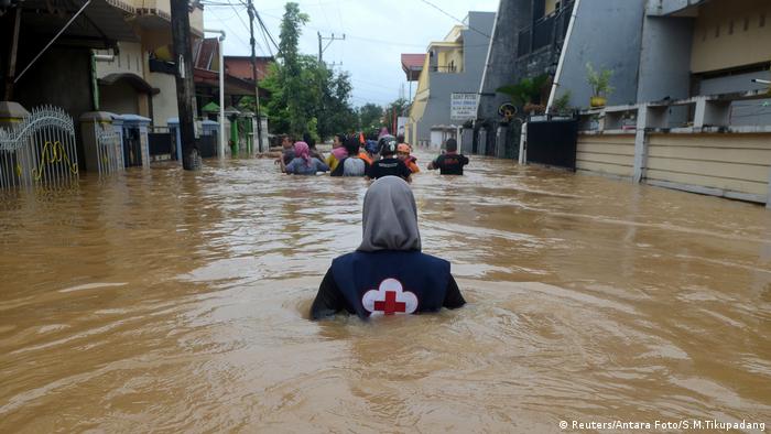 A apparent Red Cross worker back to the camera stands chest-deep in brown water in Indonesia's Sulawesi province. In the distance other persons wading. (Reuters/Antara Foto/S.M.Tikupadang)