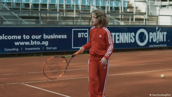 Filmszene aus Ich war zuhause, aber zeigt ein Kind im Trainingsanzug auf einem Tennisplatz (Nachmittagfilm)