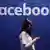 A women uses a smartphone in front of the Facebook logo