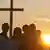 People standing below a cross at sunrise