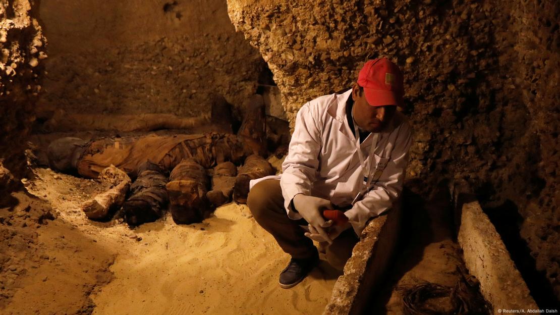 An archaeologist sits next to a mummy inside a tomb