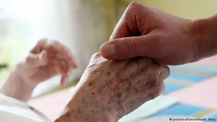 A person holds an elderly woman's hand in a nursing home