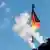 A German flag flies as emissions come out of a chimney