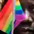 A man holds a small rainbow flag in front of his face