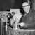 W.E.B. Du Bois steht hinter einer Reihe Mikrofone und hält ein Papier in der Hand