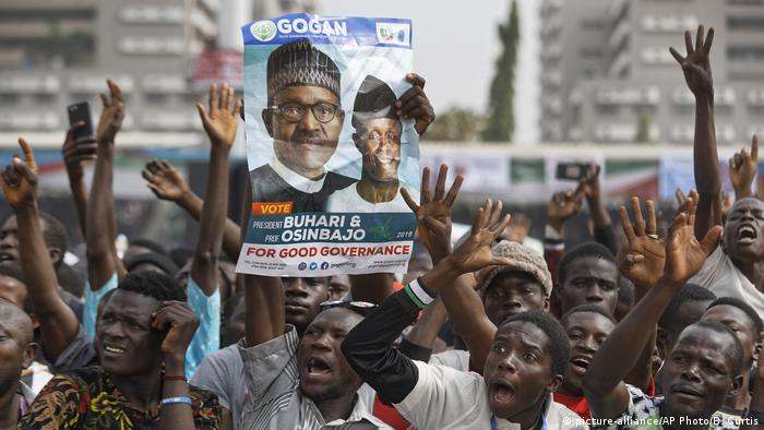 Supporters of incumbent President Muhammadu Buhari, holding a poster of Buhari and and Vice President Yemi Osinbajo, cheer as he arrives at a 2019 campaign rally in Abuja, Nigeria