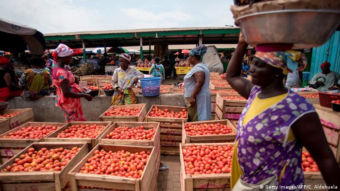 A woman sells tomatoes to a customer at her stand at the Agbogbloshie market, Accra